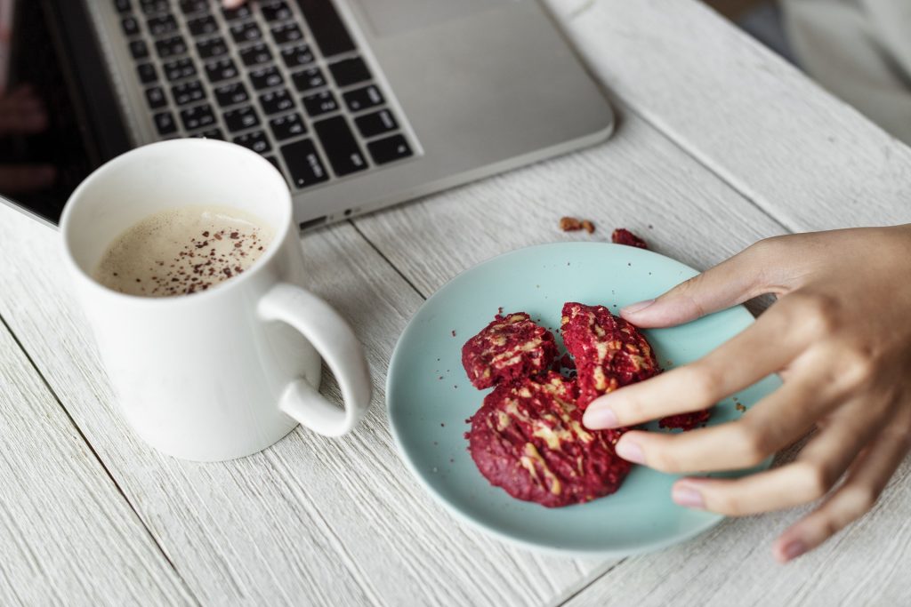 Une femme mangeant des cookies et buvant un café devant son ordinateur